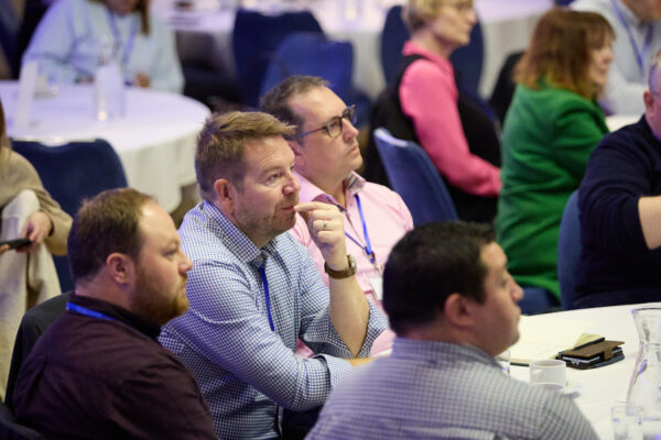 Group of conference delegates seated at round tables, watching and listening to a speaker during the INA Growth Summit 2025.